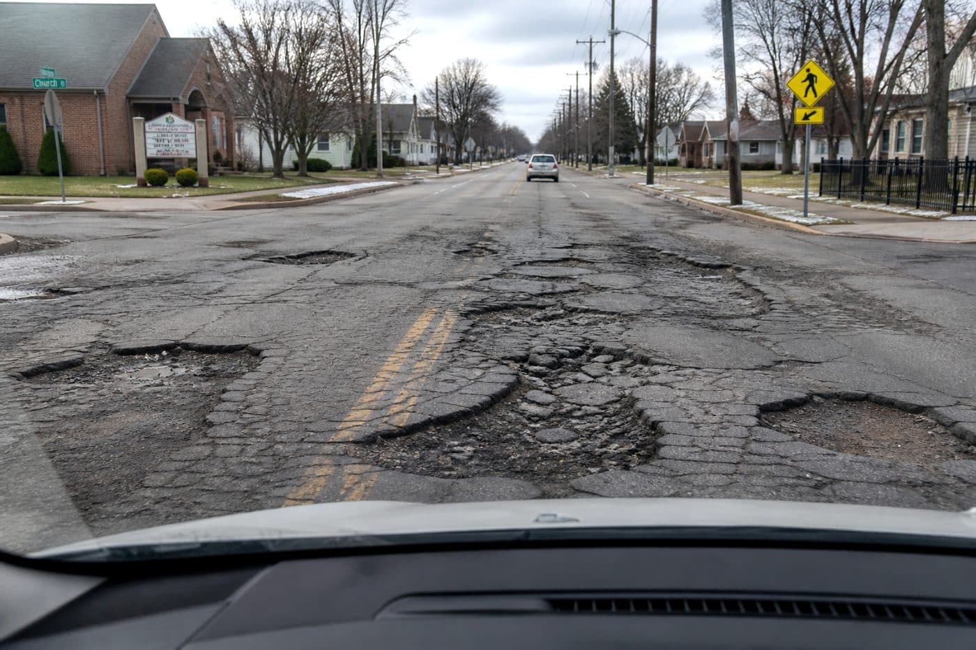 Driver-view of cracked asphalt with large potholes on a municipal road, editorial context image